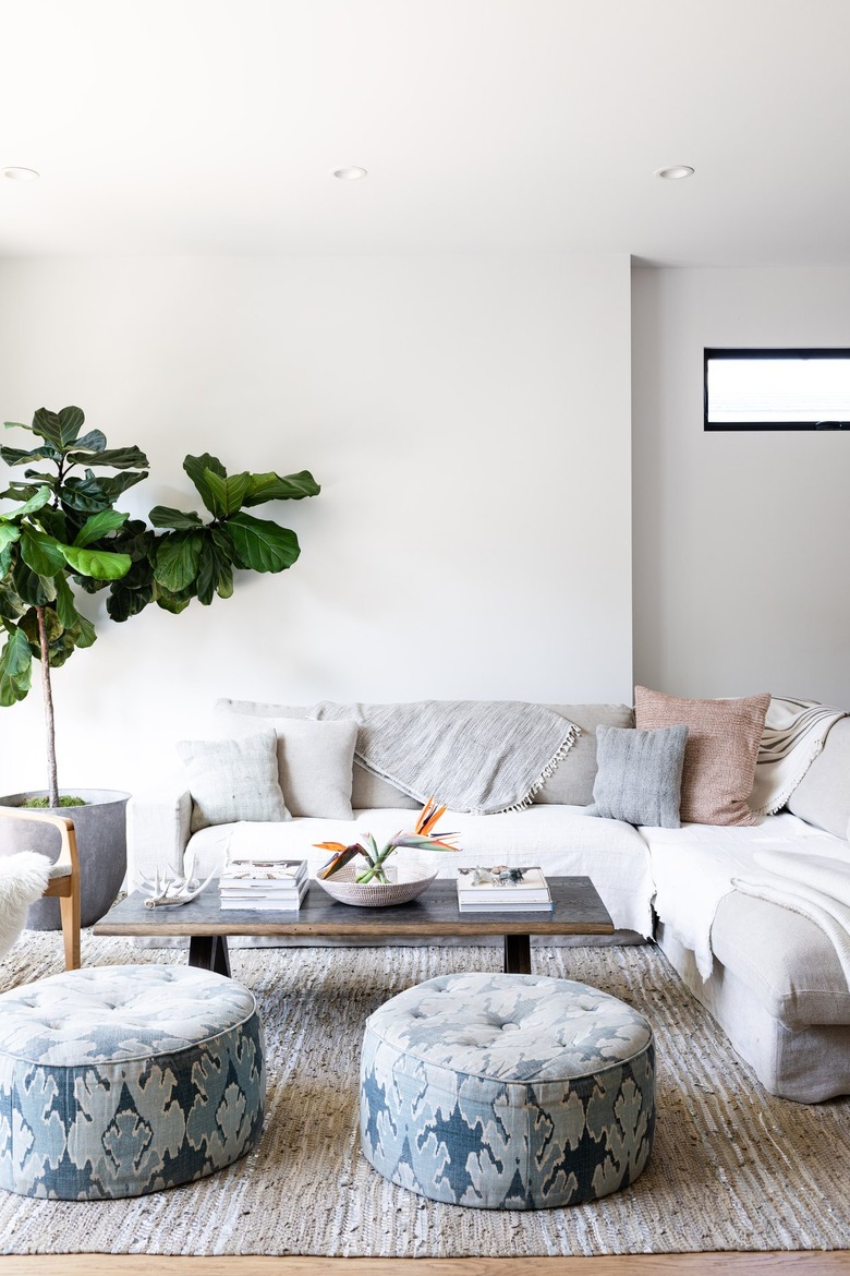 A living room sofa with pillows and blankets and ottomans on a beige rug