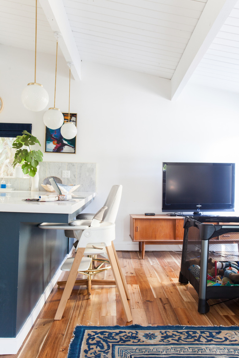 A television and a baby's crib next to a kitchen island.