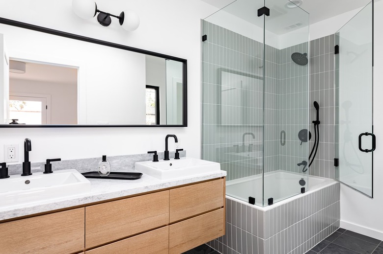 Modern bathroom with glass-walled shower over white-tiled bathtub