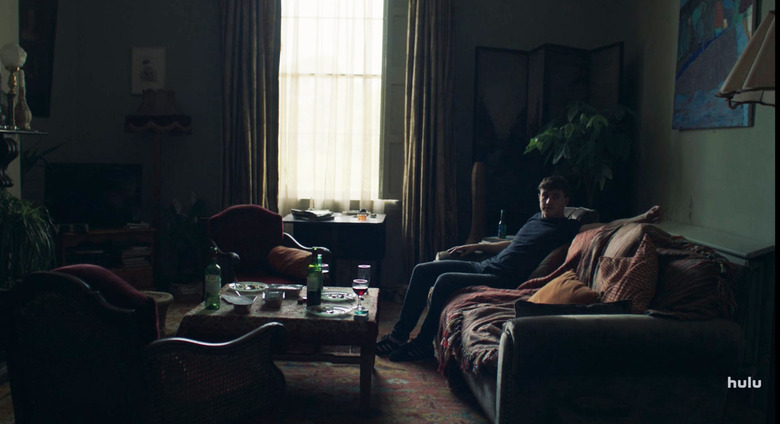 person sitting on dark couch with curtains and coffee table nearby