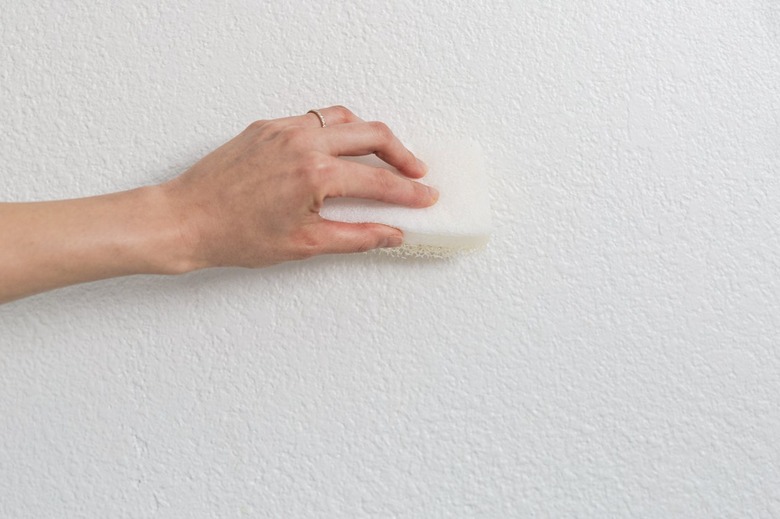 A hand holding a sponge against a wall