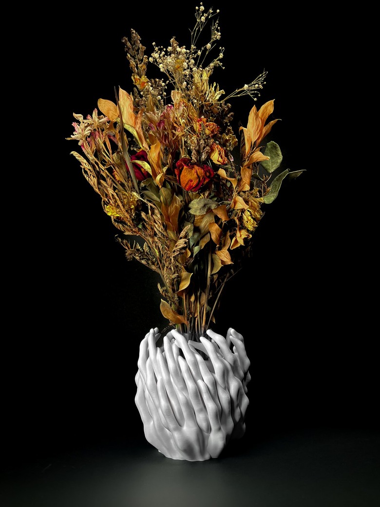 A white base holds an autumnal bouquet of roses and other flowers. The surface of the vase is jagged