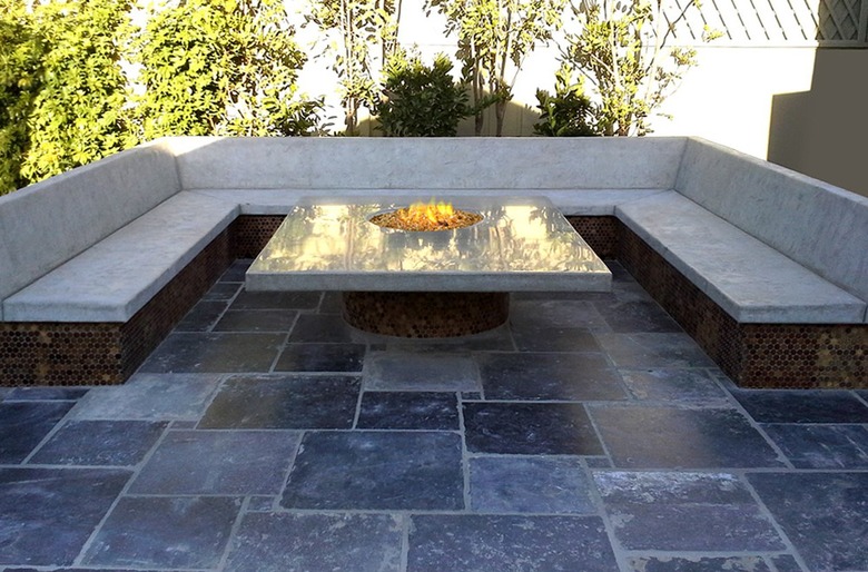 A modern gray square stamped concrete patio with a glass fire pit and a concrete bench
