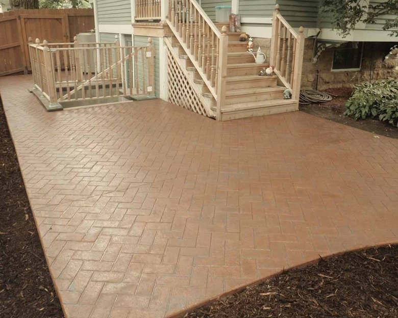 A herringbone patterned stamped concrete patio below a stairwell