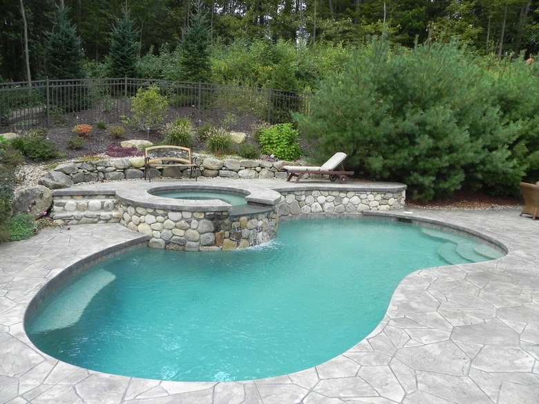 A freeform pool surrounded by a light gray stamped concrete patio