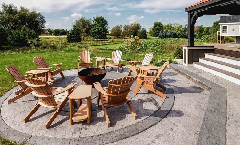 An expansive stamped concrete patio with a circular border that has several Adirondack chairs around it
