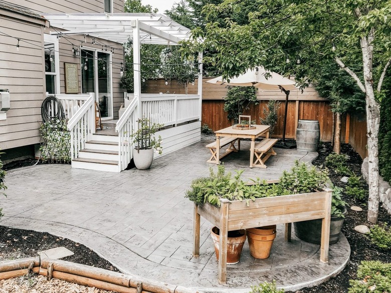 A light gray stamped concrete patio with a potting table and a picnic table