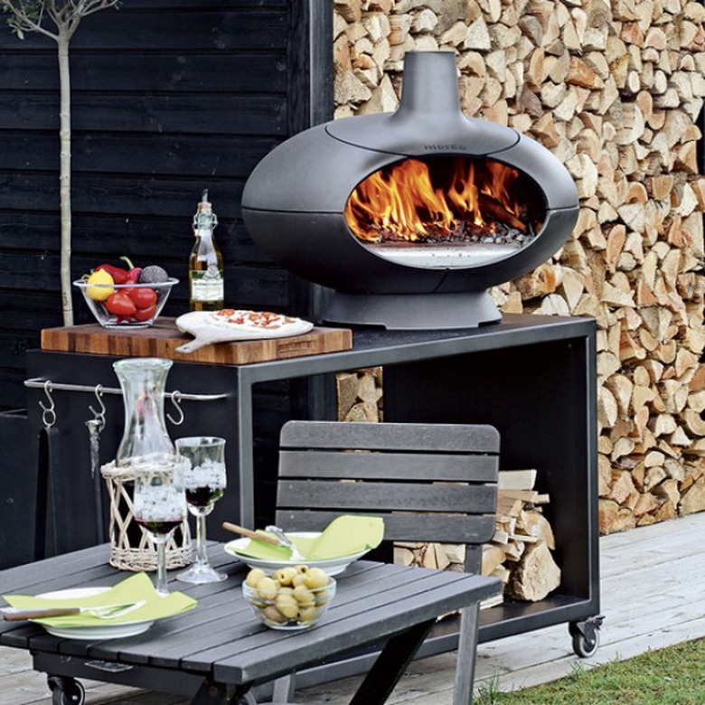 small outdoor kitchen idea with grill and pizza oven next to chopped wood