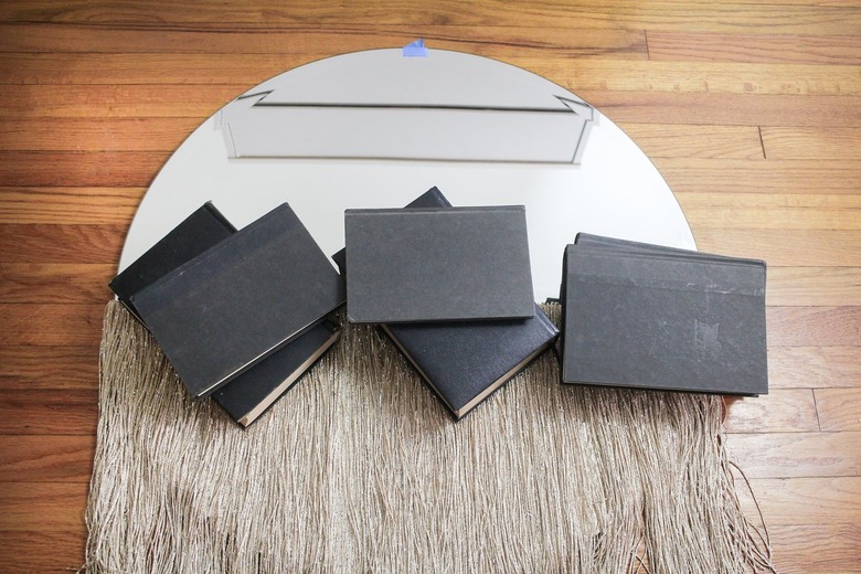 Books holding down curtain fringe on round mirror