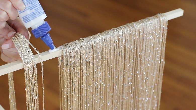 Hand placing glue on wood dowel for neutral fringe curtain panels