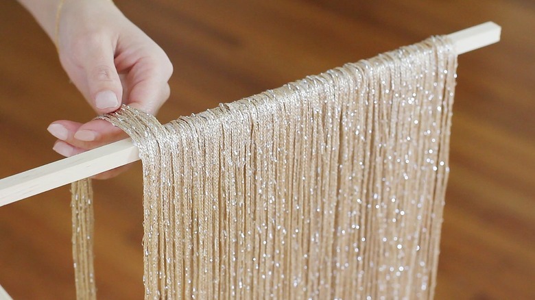 Hand placing neutral fringe curtain panels on wood dowel