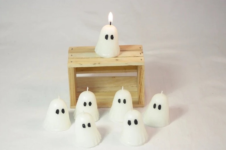 Seven tiny candles shaped like ghosts with ovular eyes. There is a small wood pallet behind six of the ghosts