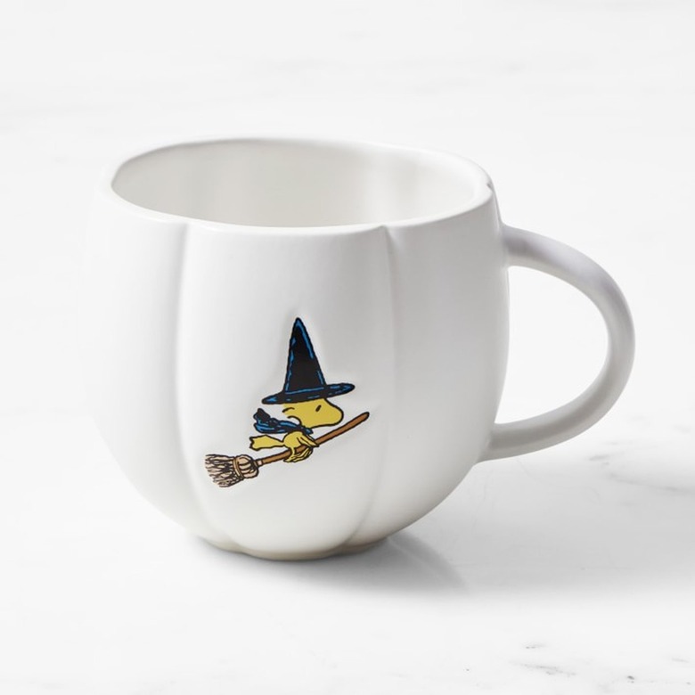 A white pumpkin-shaped mug with the Peanuts character Woodstock a yellow bird flying on a broomstick while wearing a witch's hat and cape.