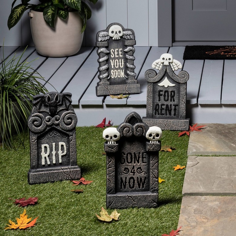 Four foam gray tombstones in a front yard and on a light blue-gray front porch. Three have skulls on them