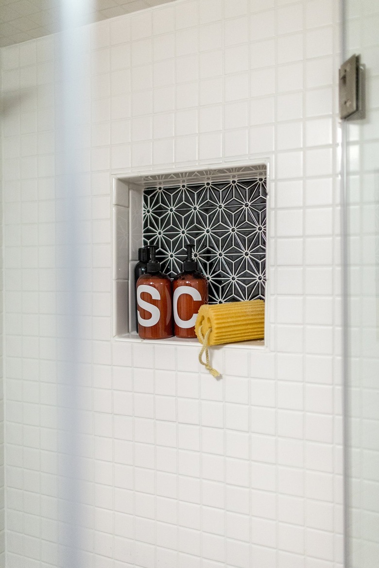 White tiled shower with a black-white geometric tile in shower niche