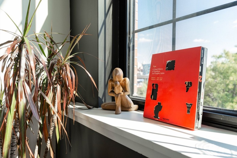 Red book on white countertop with plants against black wall with black-framed windows