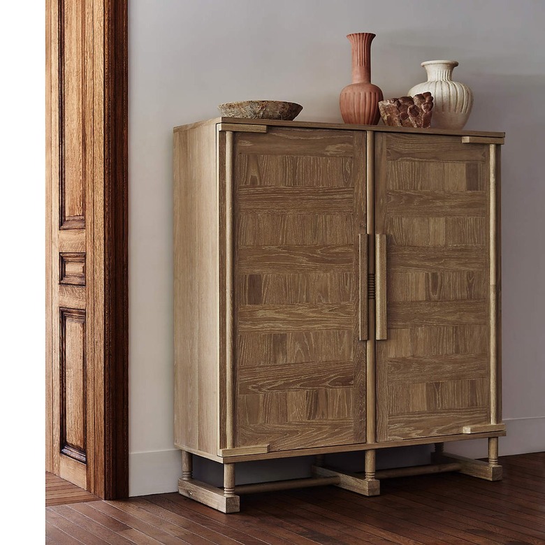 Oak wooden storage cabinet on a hardwood floor topped with various vases