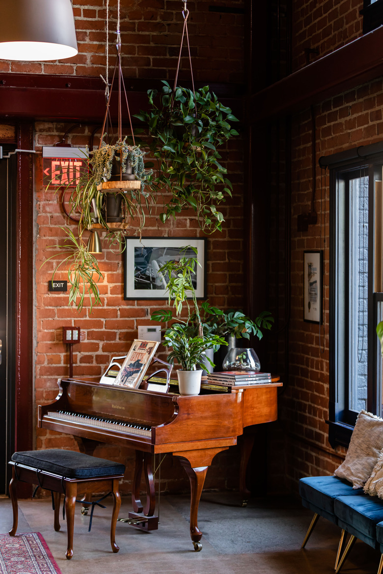 Mini grand piano in brick-wall corner below hanging plants