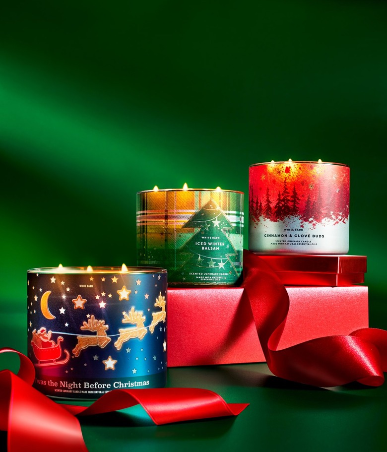 A stack of red presents against a green background with three Bath and Body Works 3-wick candles displayed: Twas the Night Before Christmas