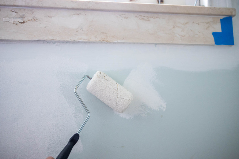 Painting white paint onto blue wall with a roller