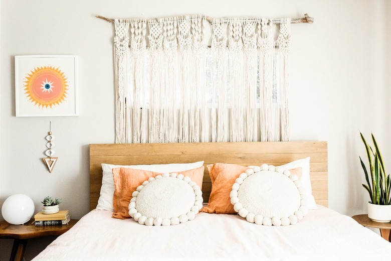 A bed with a wood headboard and peach-white pillows. A macrame curtain behind