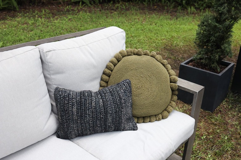 Dark gray lumber pillow and round green pompom pillow on outdoor couch