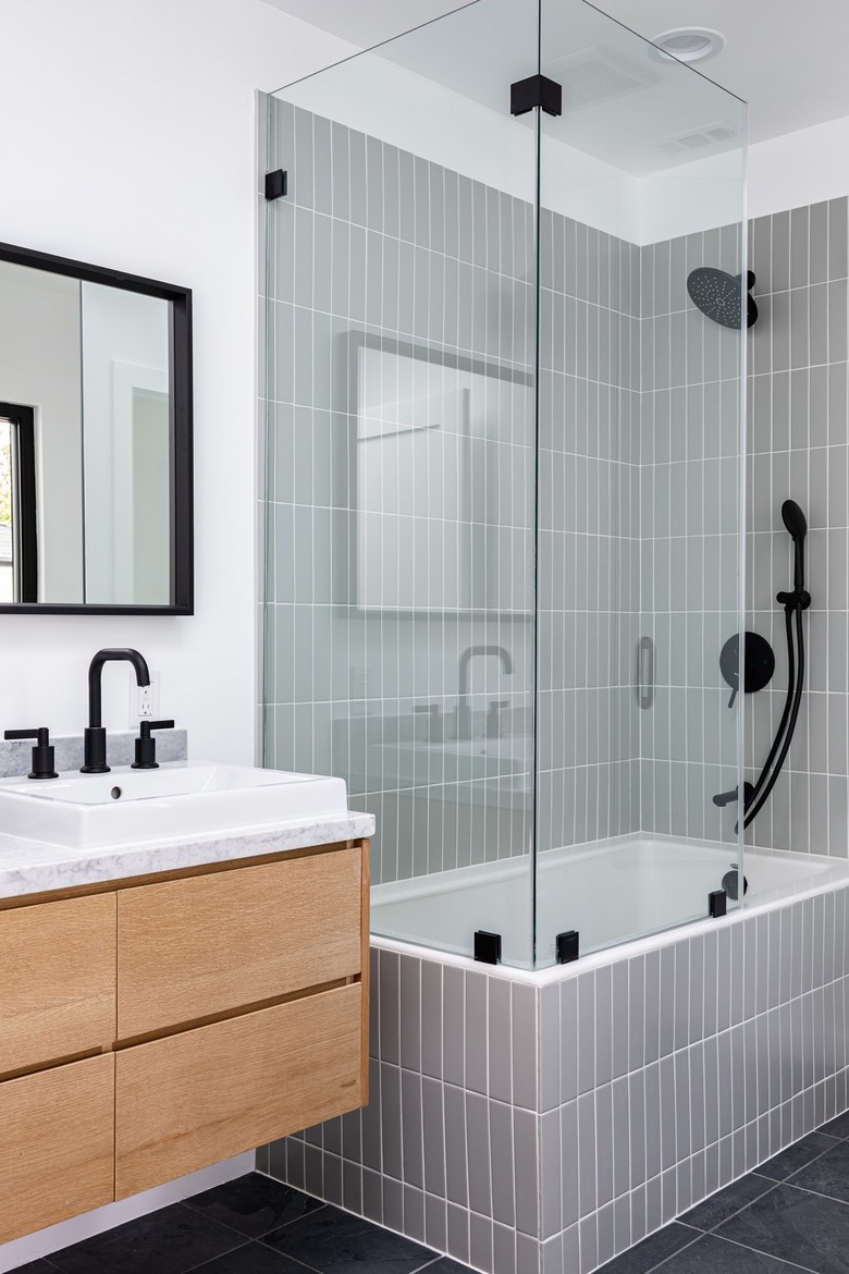 Modern bathroom with glass-walled shower over white-tiled bathtub