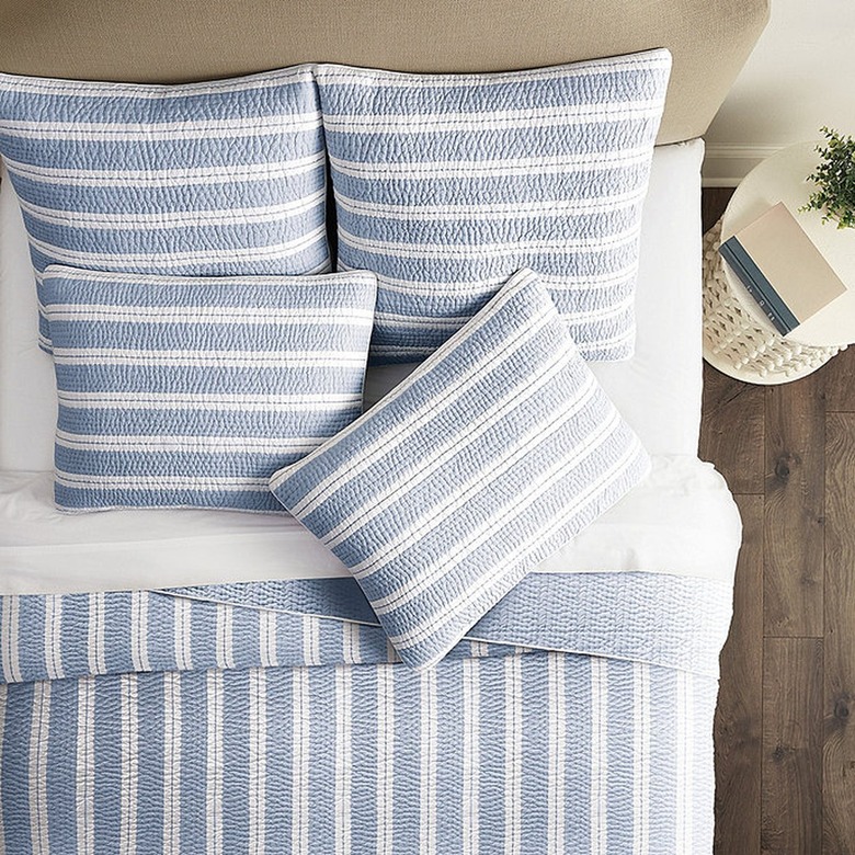 Blue quilt with white stripes on bed with beige headboard and white bedding