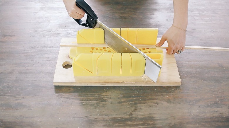 Hand using saw to cut wood dowels on mitre box