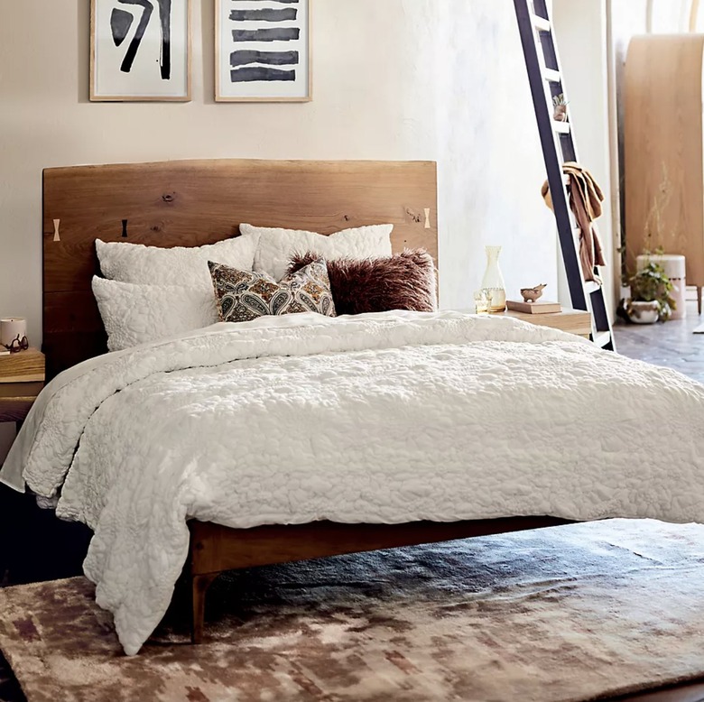 white quilt in a room with a wooden bed frame and white walls