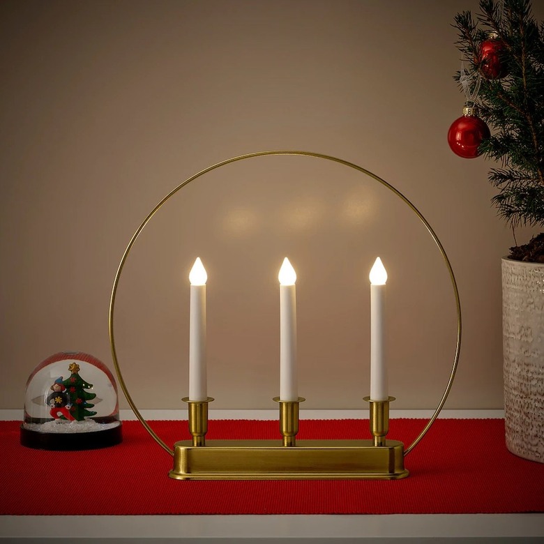 A gold candelabra featuring three LED white candles surrounded by a circle of hold wire.