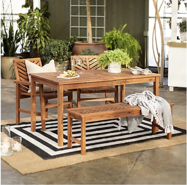Wooden outdoor dining set on black and white rug on back pation surrounded by plants