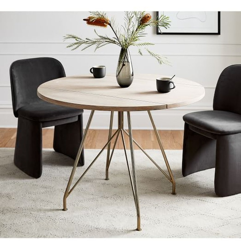 Image of a mid-century modern round dining table with brass colored legs. Two black chairs surround the table