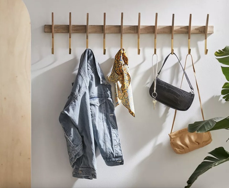 midcentury modern light wood coat rack with gold hooks against a white wall with coat