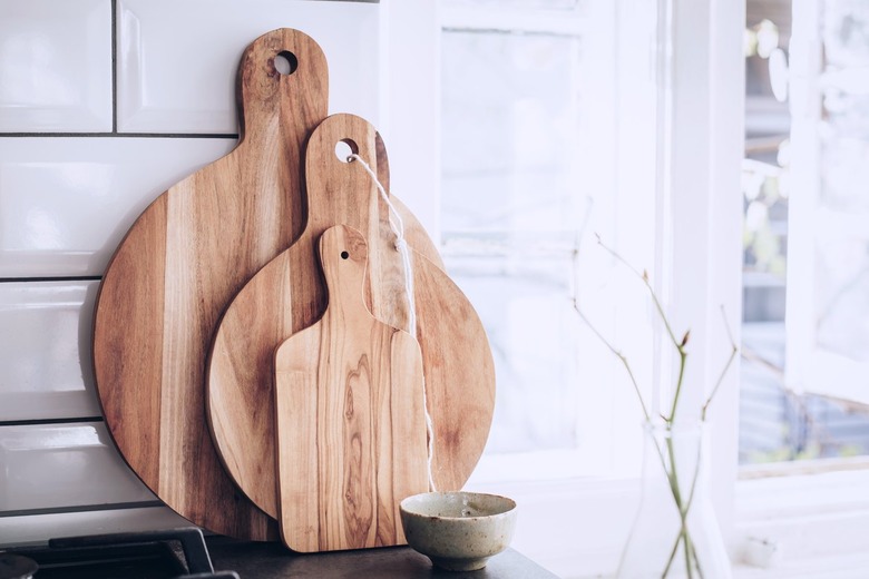 Three wood cutting boards and small cup on stone countertop leaning against tile kitchen backsplash next to white windowsill