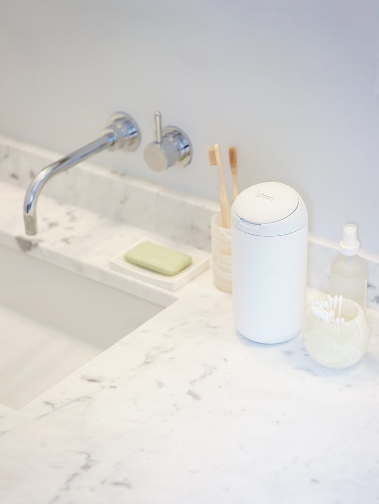 A white container of biom wipes rests on a white marble bathroom sink next to a small