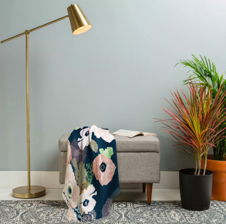 ottoman with floral blanket and lamp and plants nearby