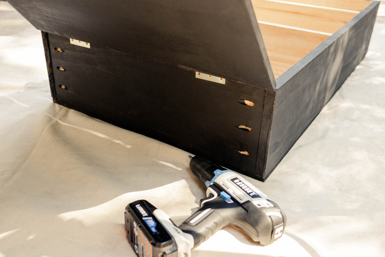 Two brass hinges attached to bottom of cabinet with HART drill