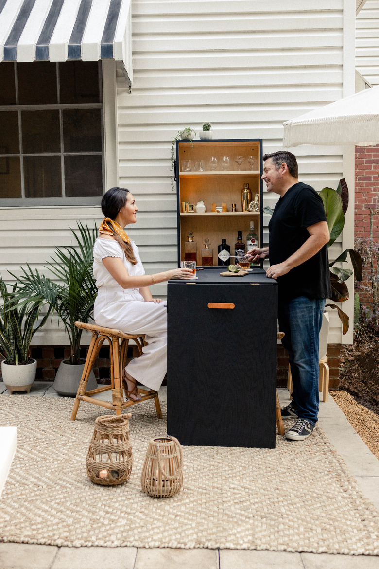 Woman seated and man standing at outdoor Murphy bar on patio enjoying cocktails