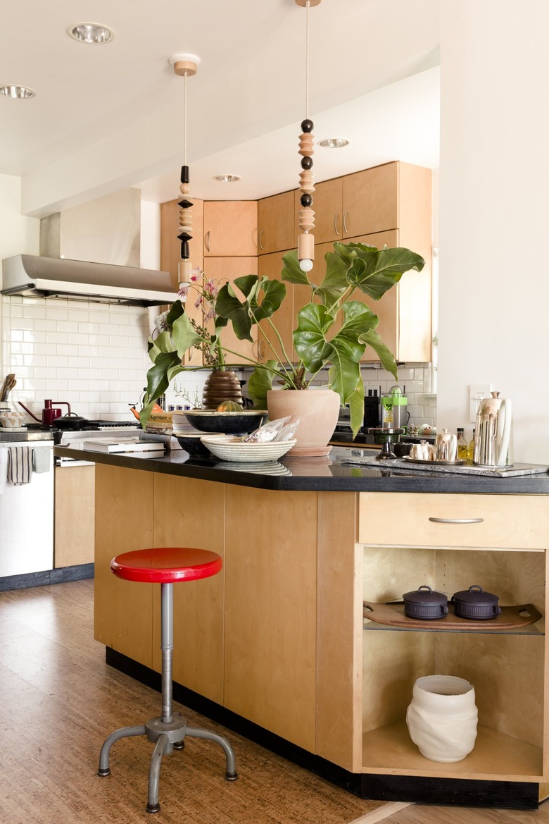 Red stool at a light wood kitchen island with black counter. Black and white dishes