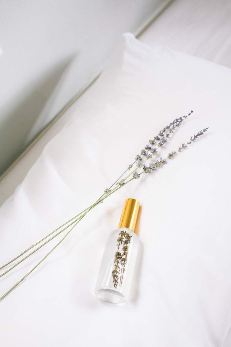 DIY pillow mist in glass bottle on top of pillow with three sprigs of lavender