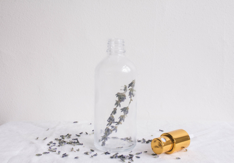 Two sprigs of lavender inside a small glass bottle with gold top on the side