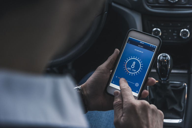 Man in car adjusting smart home device via smartphone