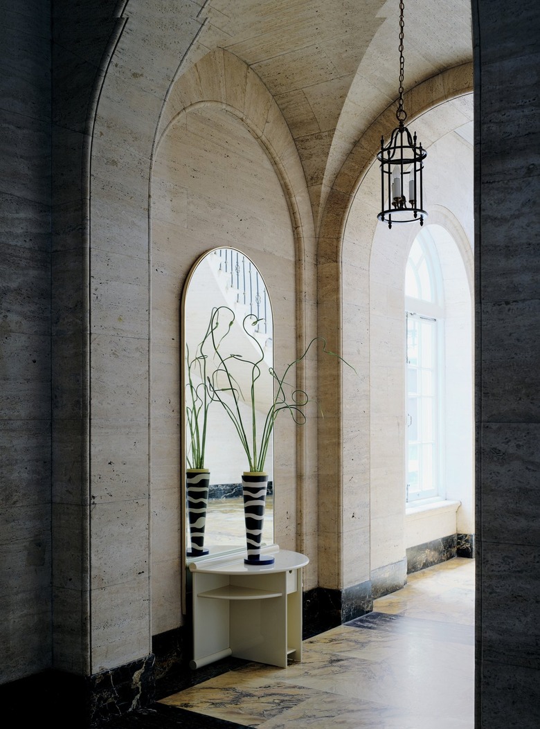 A high-gloss ivory nightstand that has a pull-out drawer that sits between horizontal upper shelves