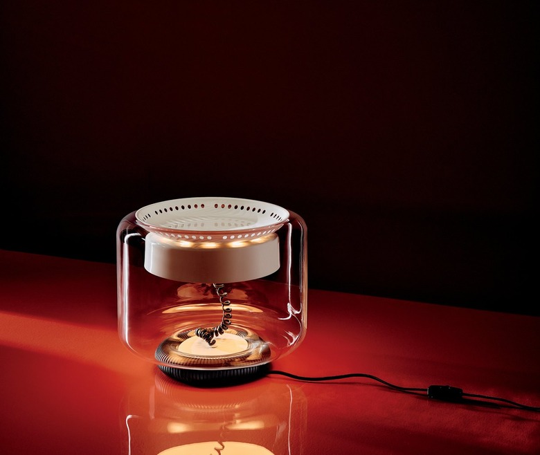 A clear glass shade resting atop a rubberized base surrounds a perforated frame coated in ivory enamel; four bulbs provide abundant light for reading