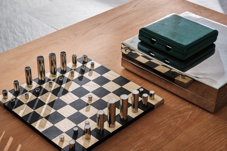 A simple chess board on a wood table featuring abstract stainless steel chess pieces that stack within each other