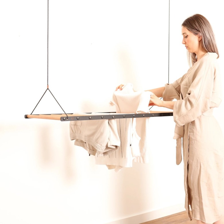 Woman putting white clothes on a drying rack that is hanging from the ceiling