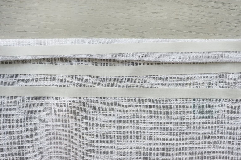 Three strips of no-sew hemming tape placed at top of fabric