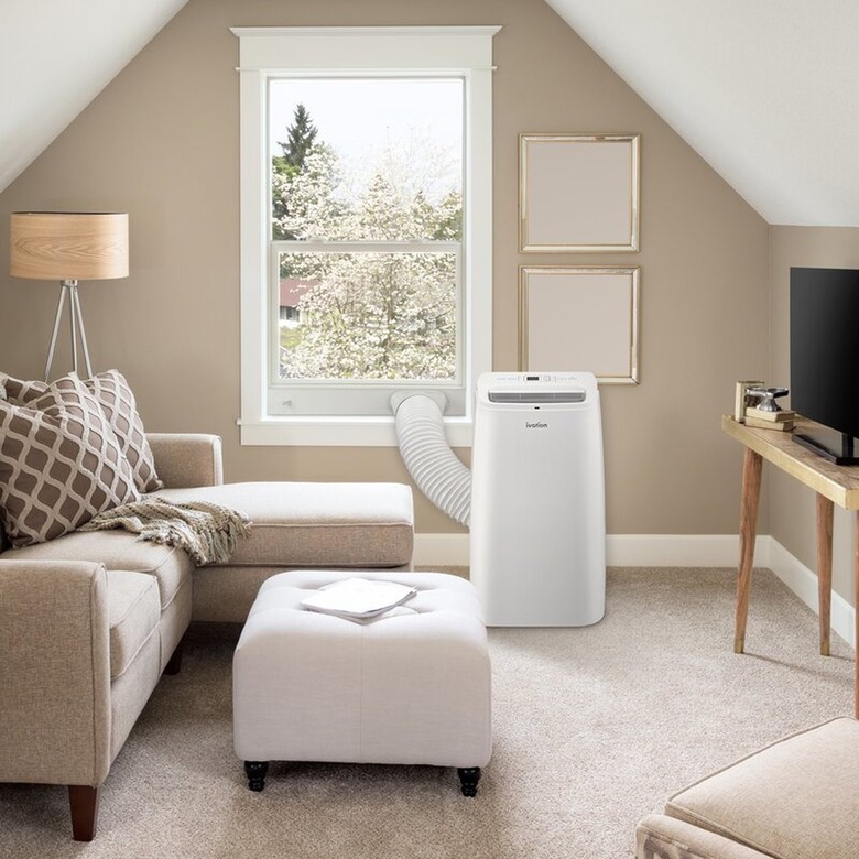 A white portable A/C in a living area with carpet and a tan sectional