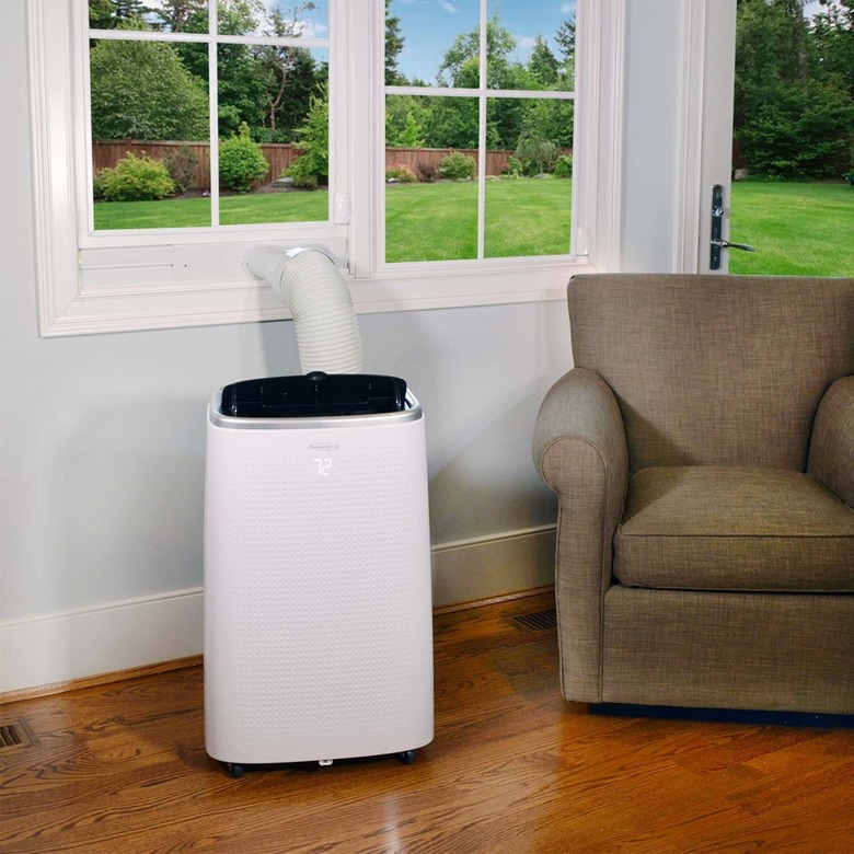 A white portable A/C in a living room with wood floors and a tan chair